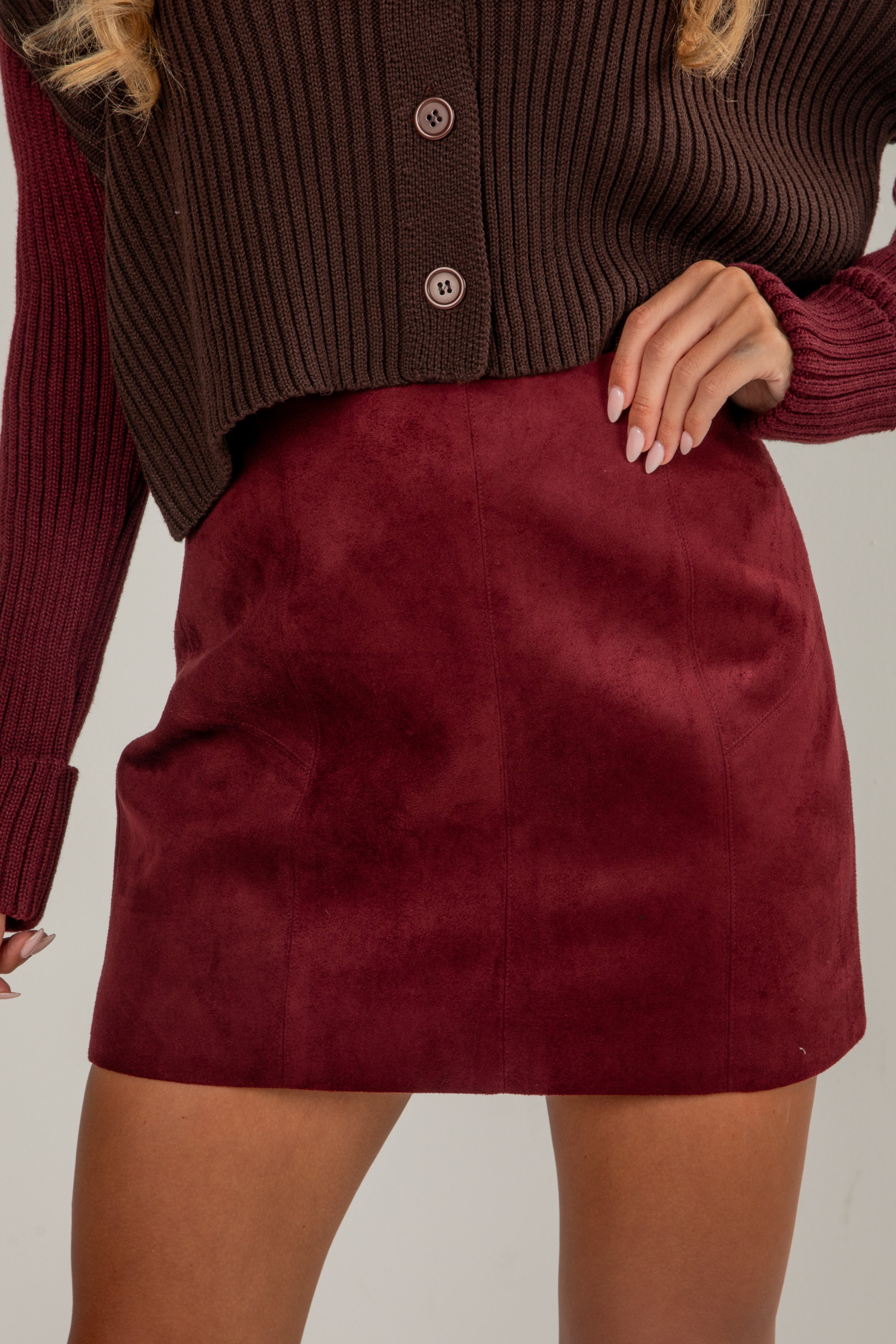 Maroon suede skirt worn with a brown ribbed sweater on a neutral background