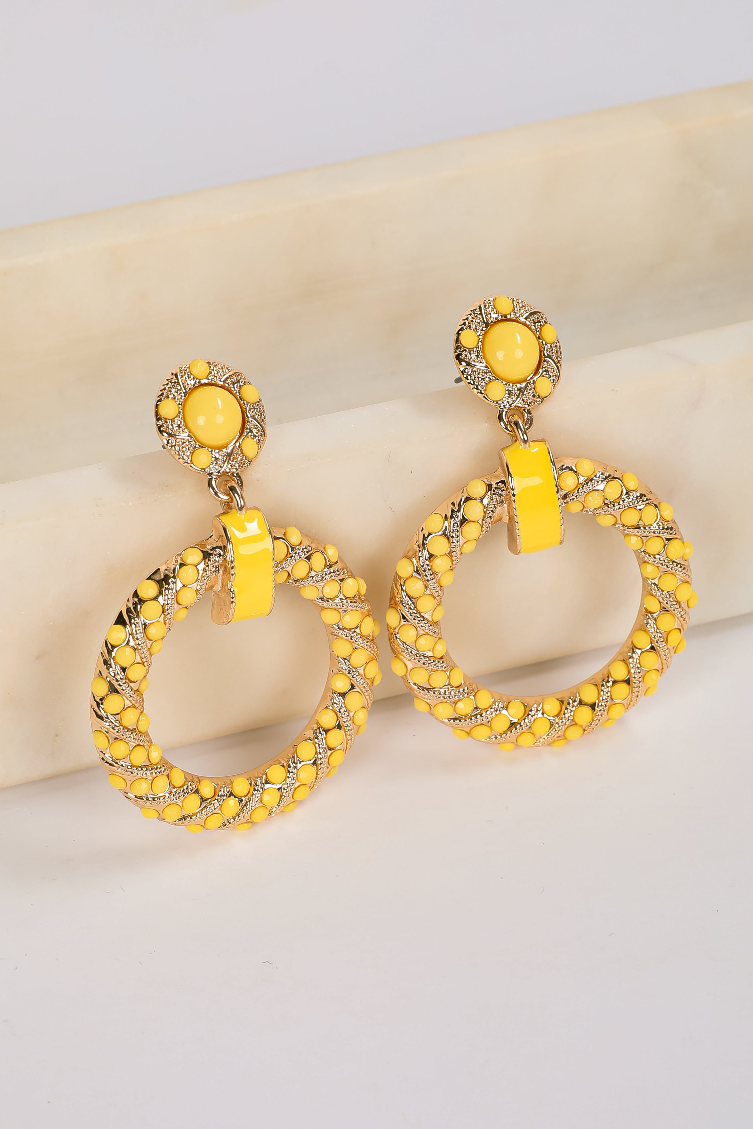 Yellow hoop earrings with intricate designs on a light background