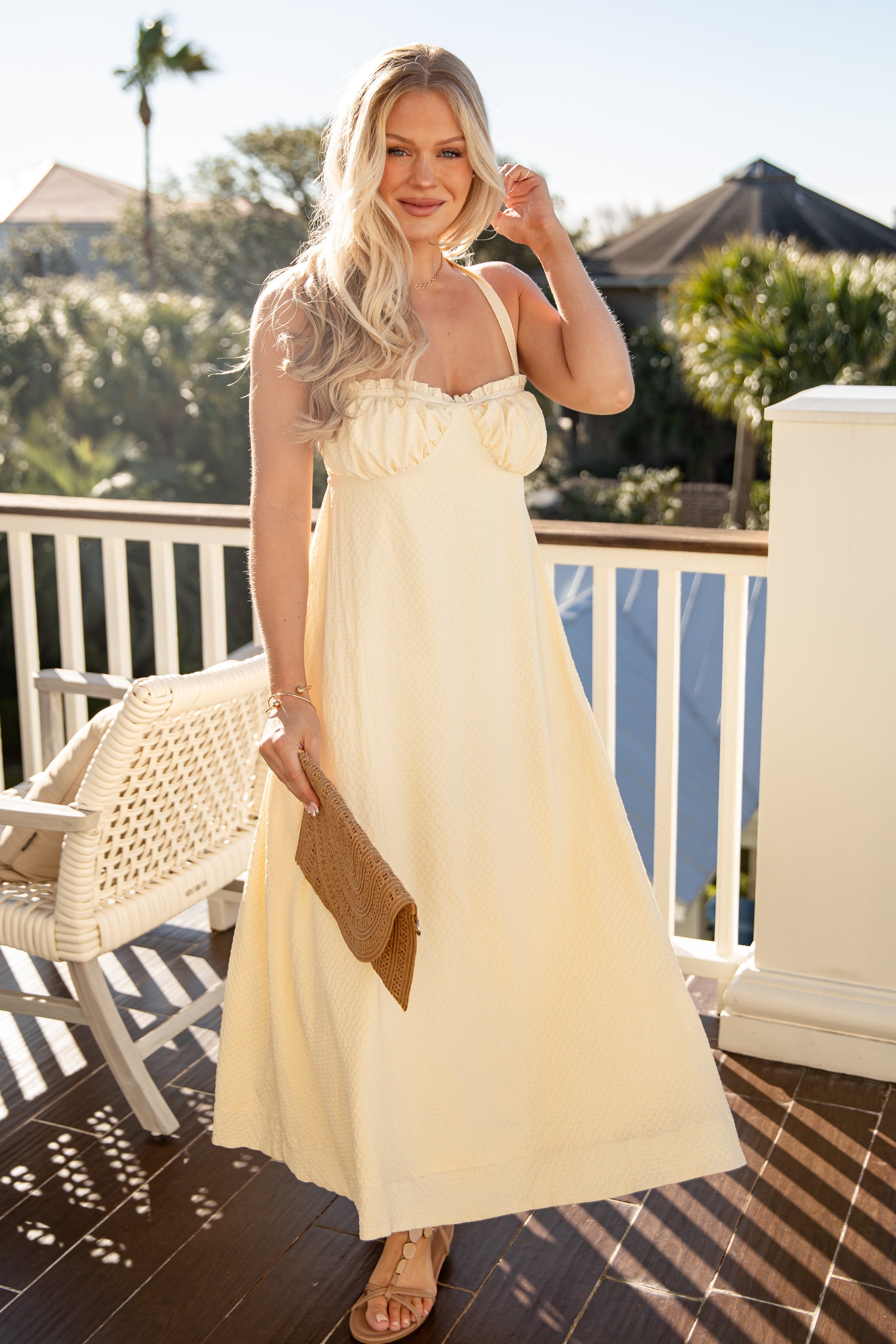 Woman in a yellow dress standing on a balcony with palm trees in the background