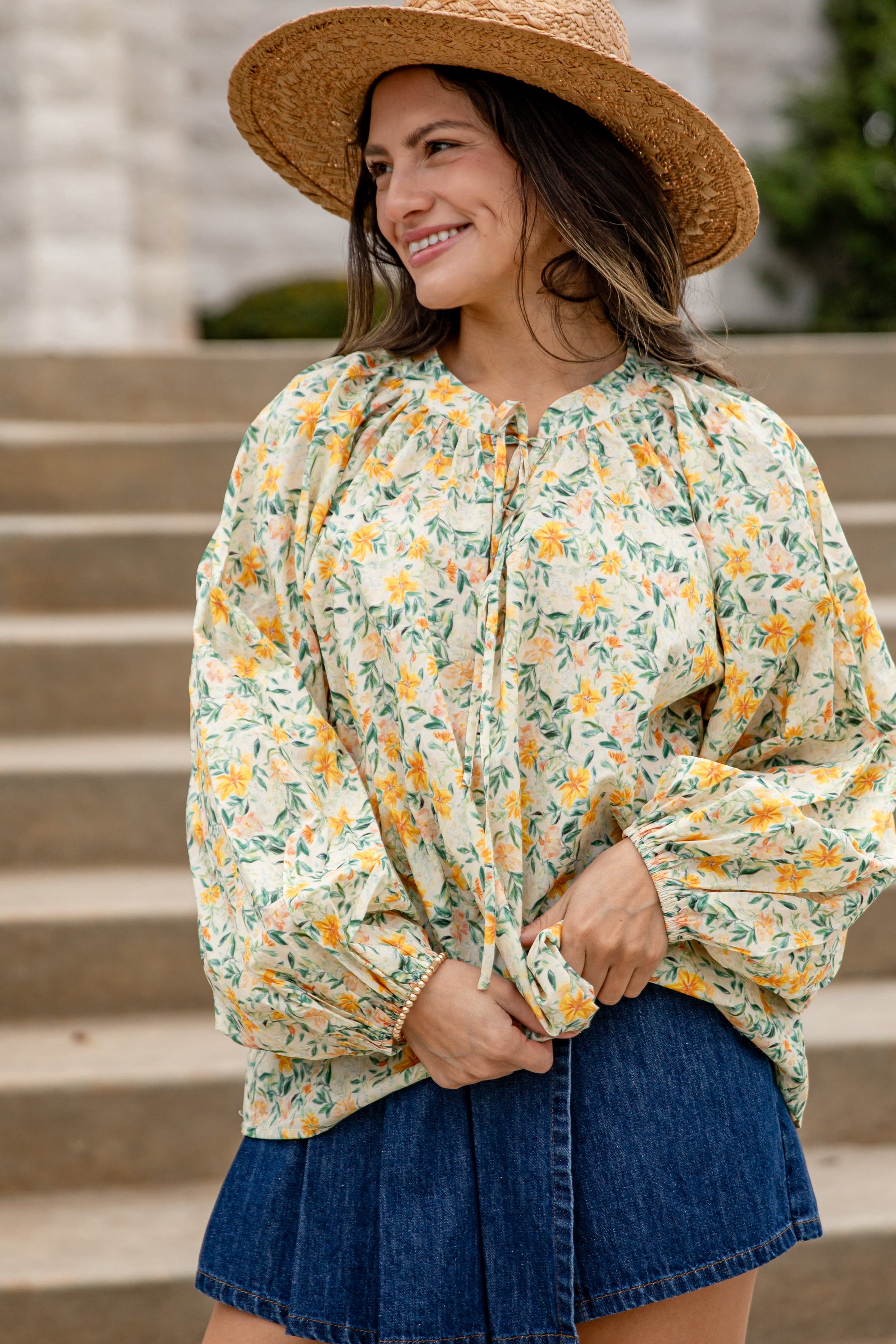 Woman wearing a floral blouse and denim skirt standing on steps outdoors.