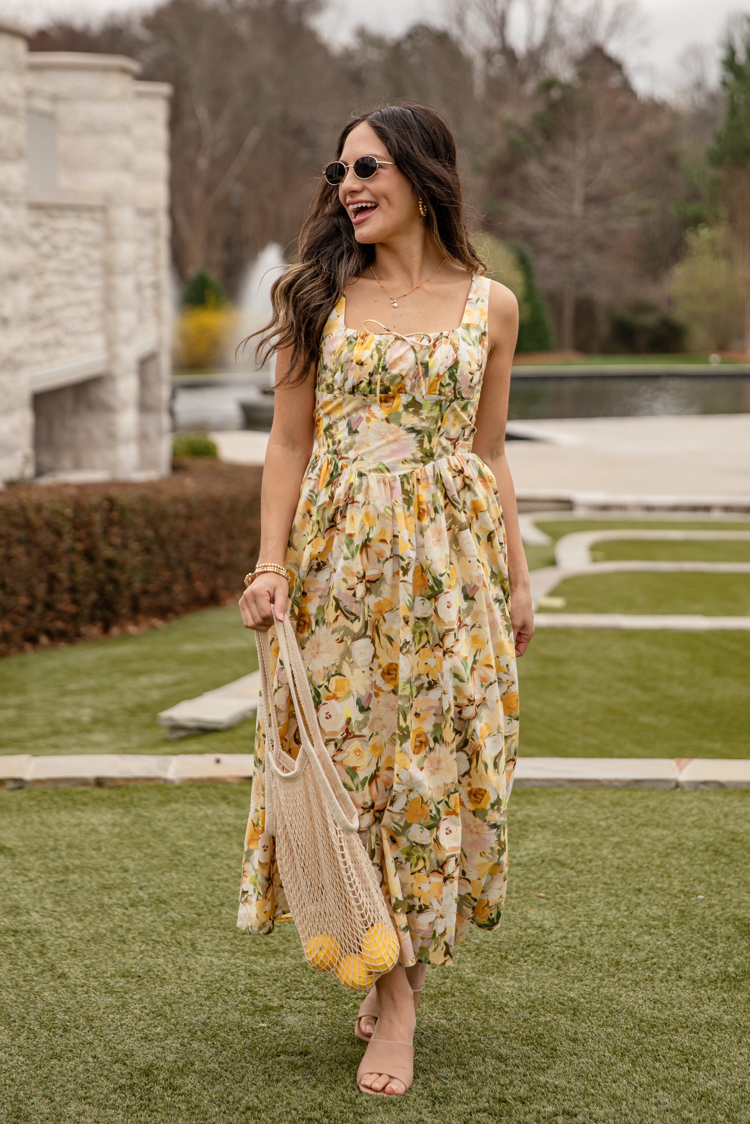 Woman in a floral dress holding a reusable bag on a grassy area.