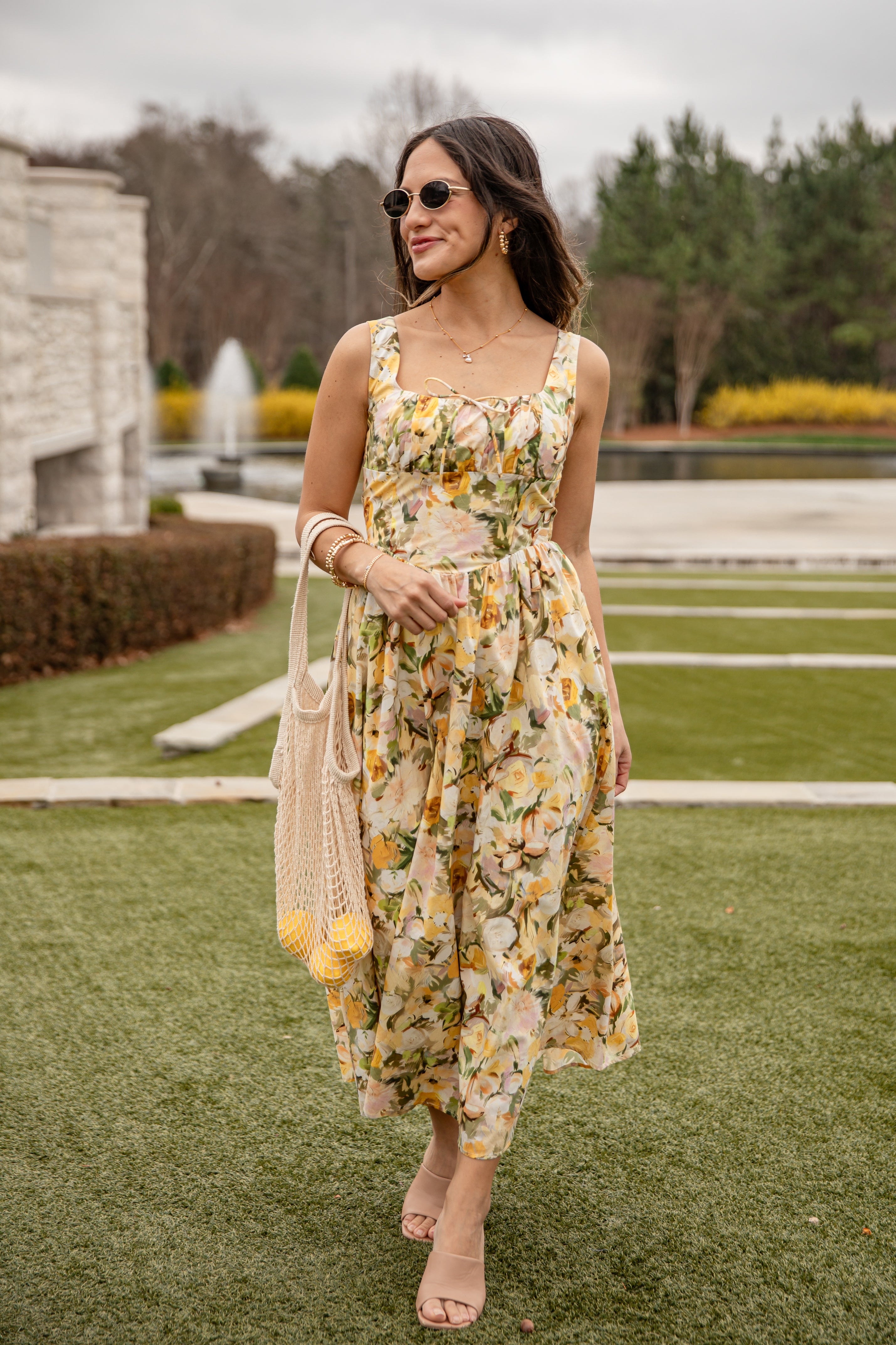 Woman in a floral dress standing on grass with a fountain in the background
