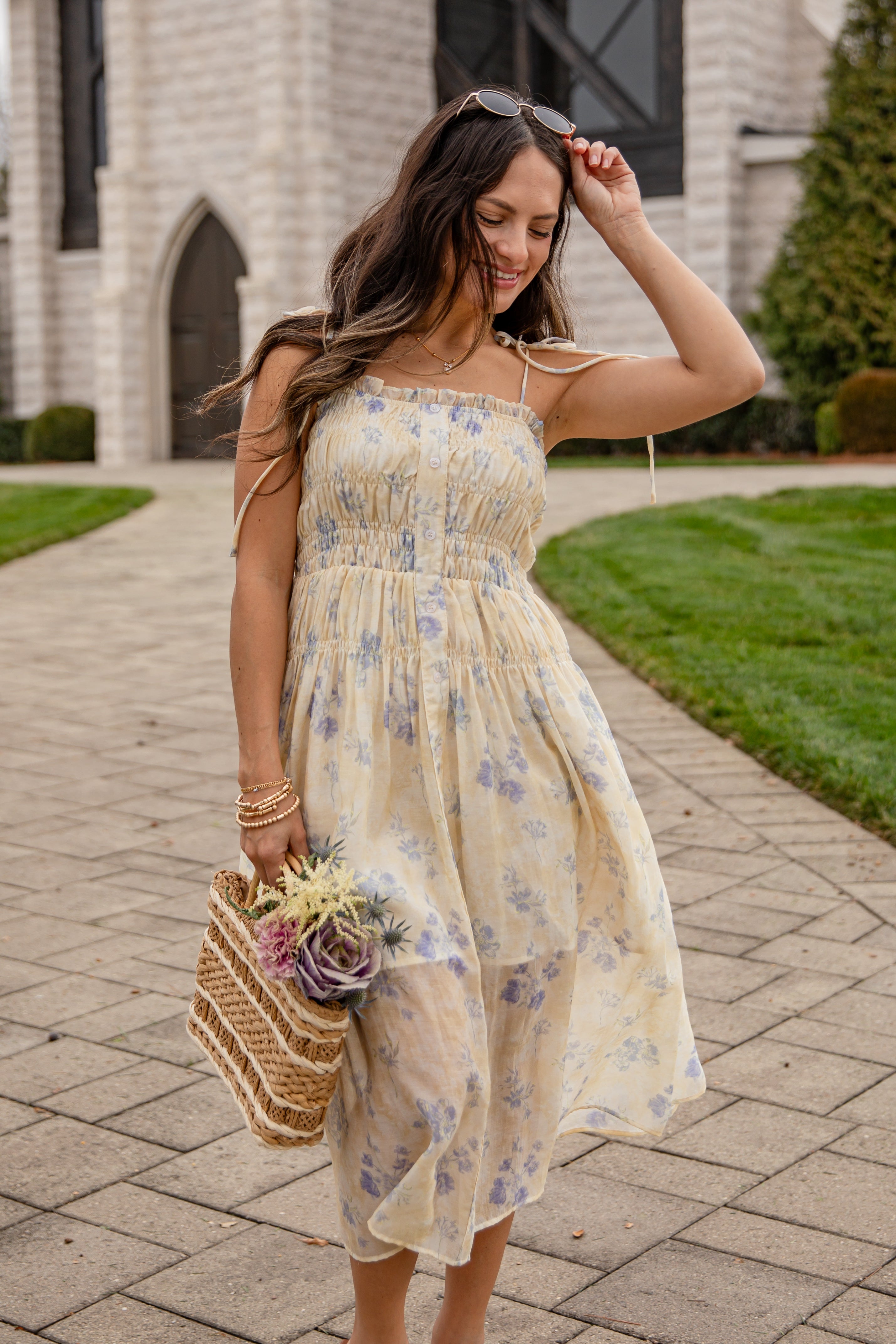 Woman in a floral dress holding a bouquet of flowers on a sidewalk.