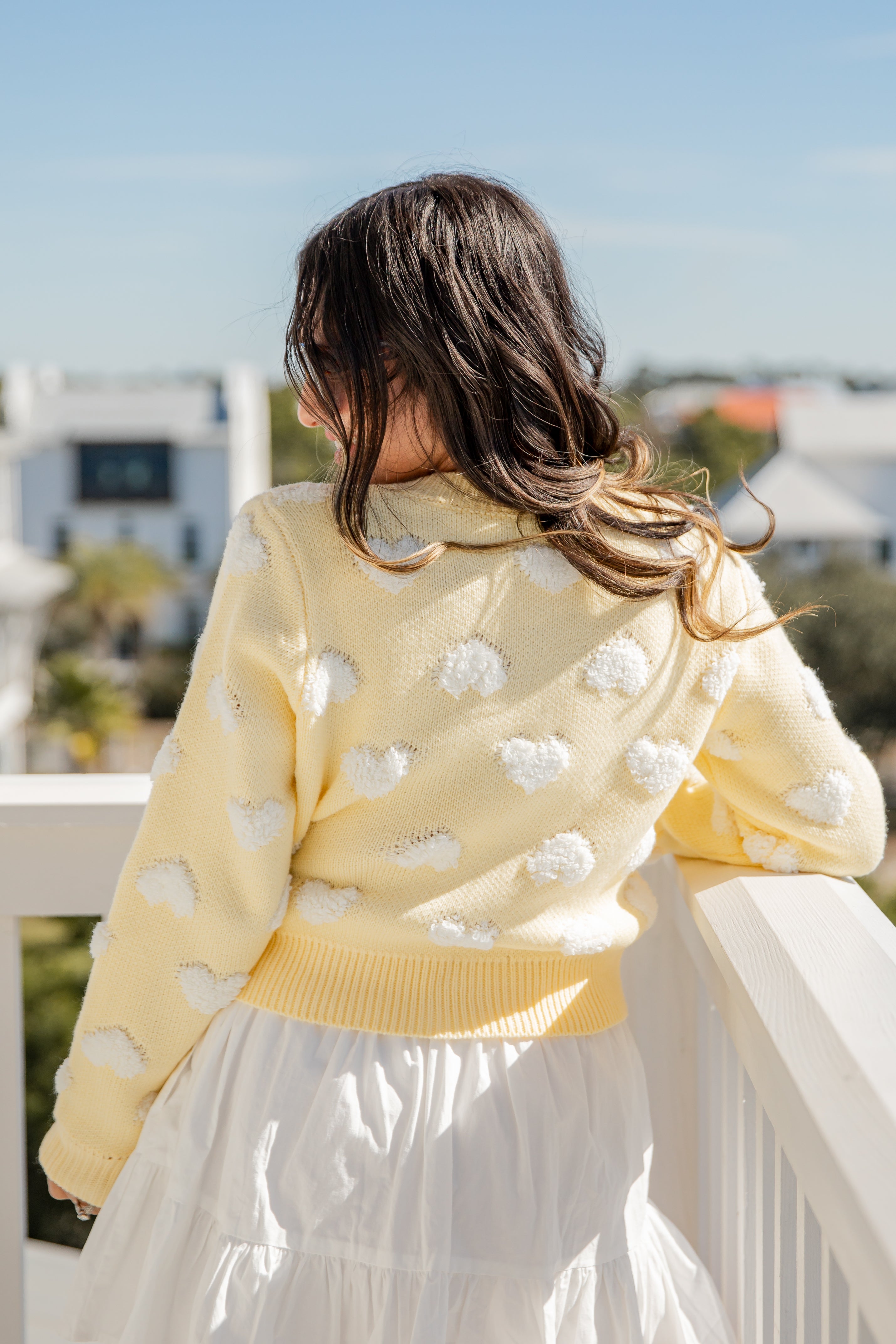 Person wearing a yellow sweater with white cloud patterns on a balcony
