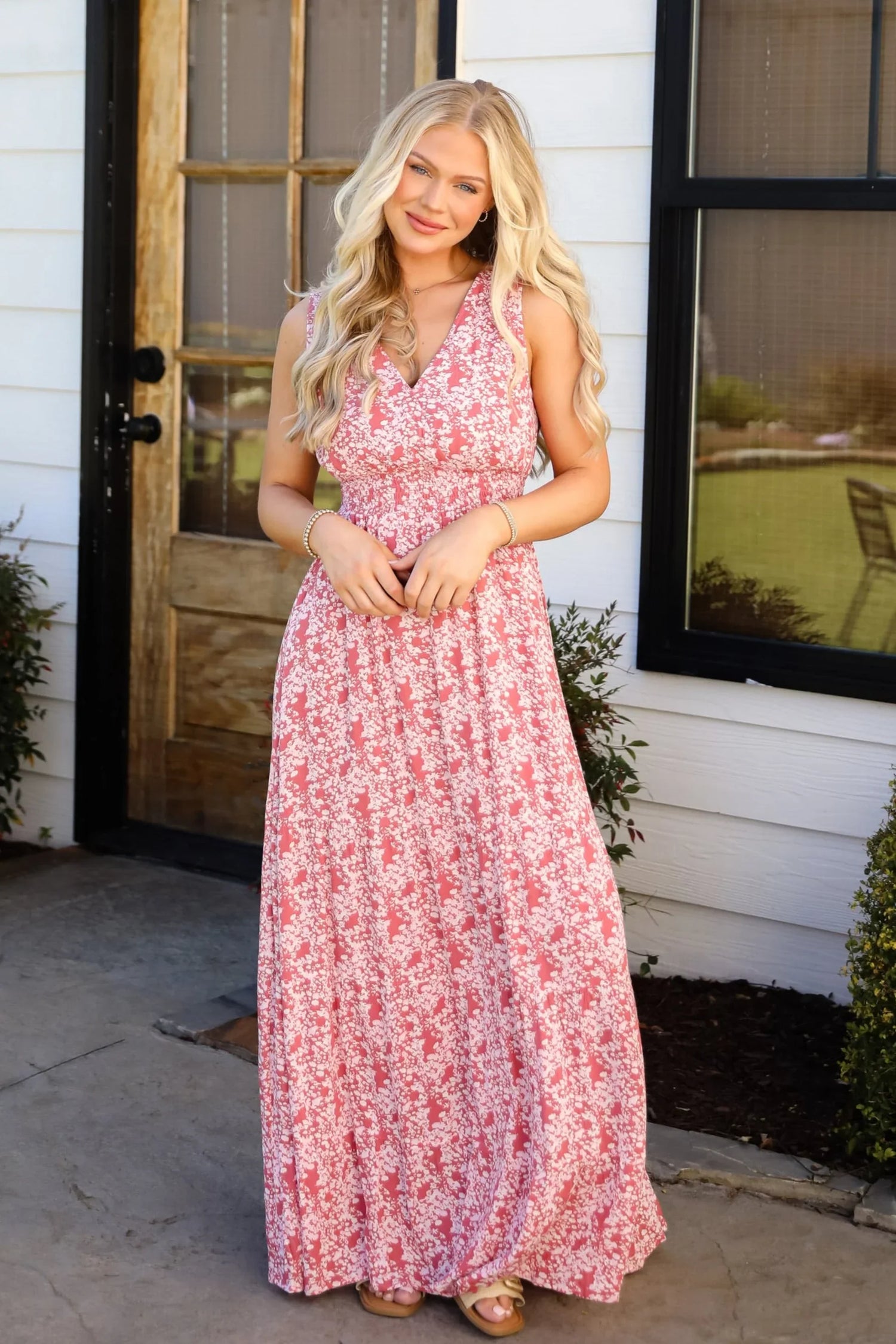 Woman with long blonde hair standing outside wearing a pink patterned maxi dress