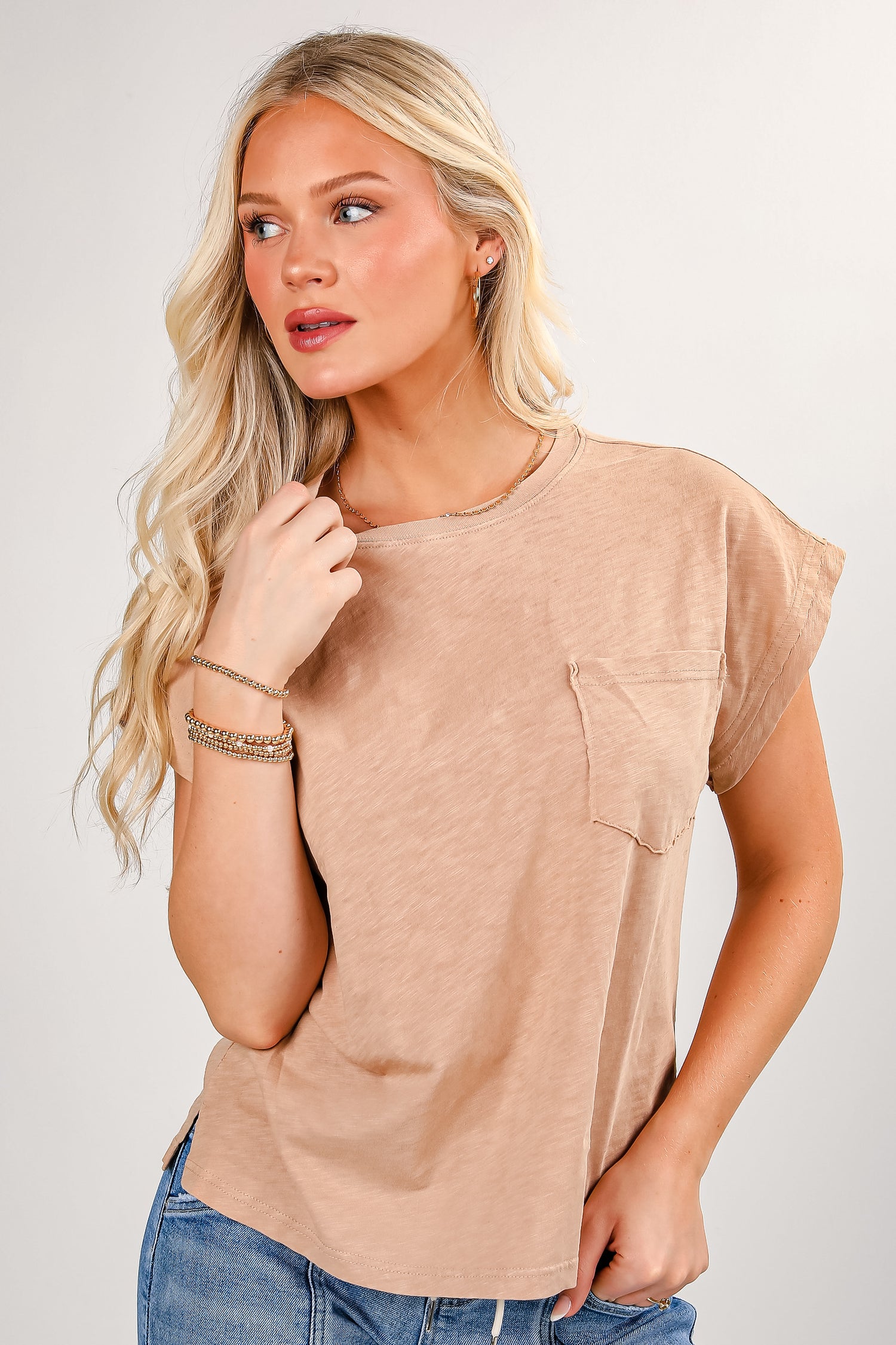 Woman wearing a beige t-shirt with a pocket and blue jeans on a plain background