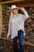 Woman wearing a checkered shirt and cowboy hat standing in front of stacked firewood.