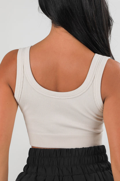 Person wearing a beige tank top and black pants on a white background