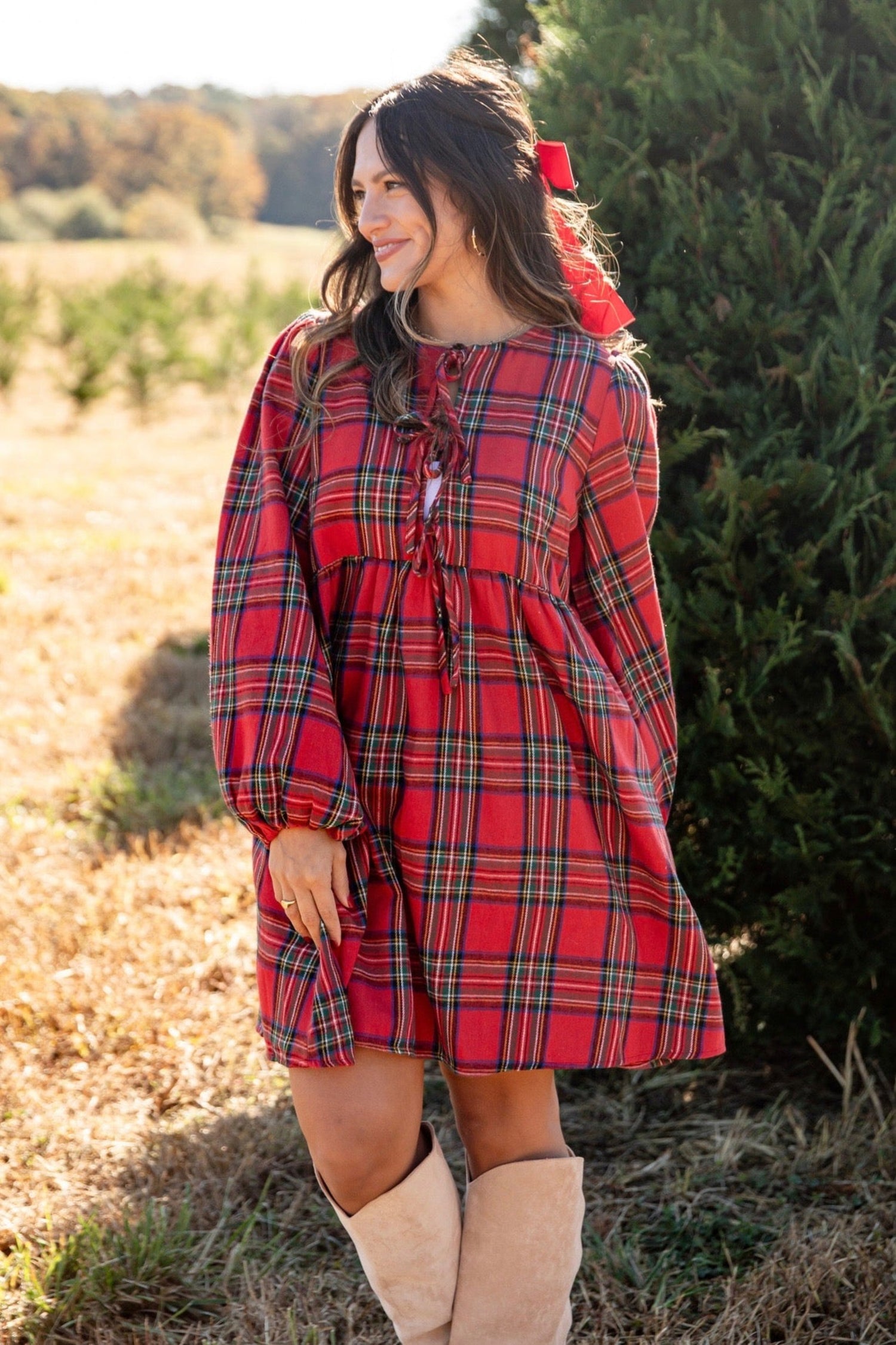 Woman wearing a red plaid dress with a bow in her hair, standing outdoors.