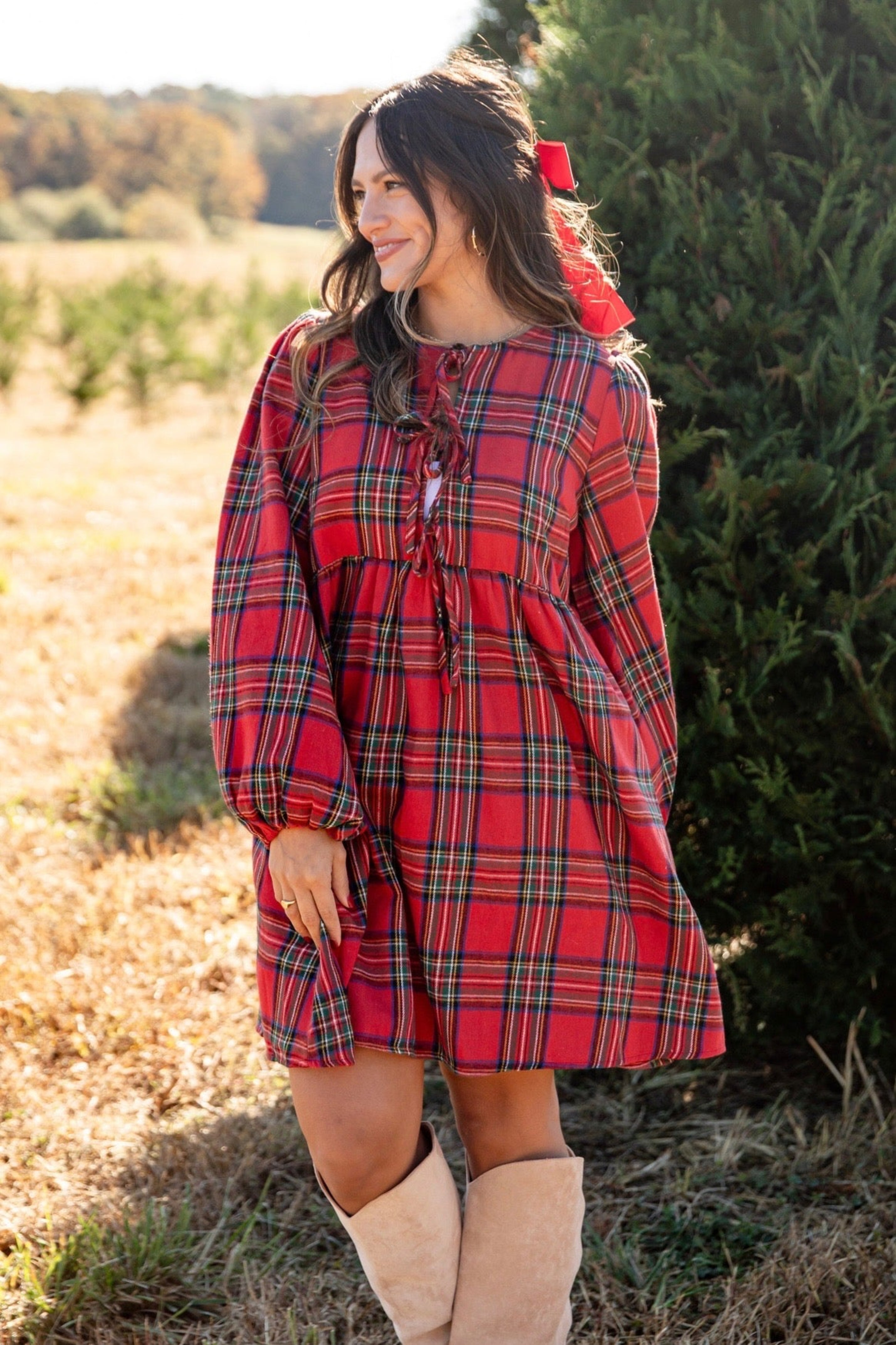 Woman wearing a red plaid dress with a bow in her hair, standing outdoors.