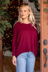 Woman wearing a burgundy sweater and blue jeans standing in a doorway with Christmas decorations.