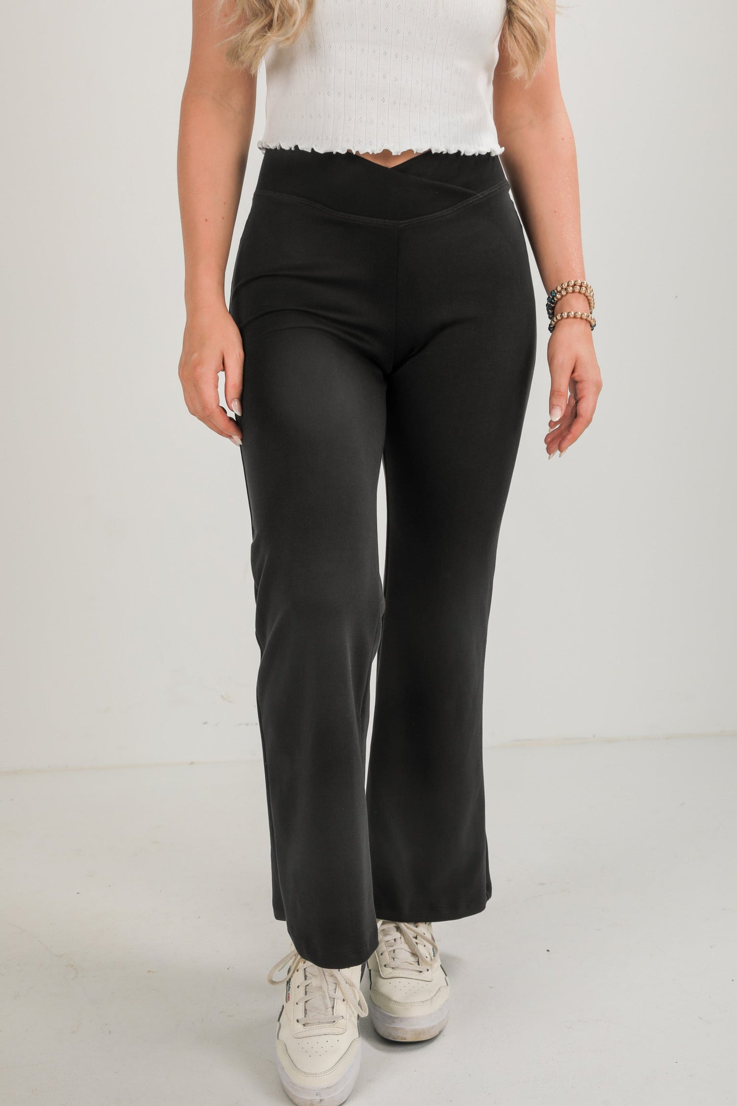 Person wearing black pants and white sneakers on a plain background