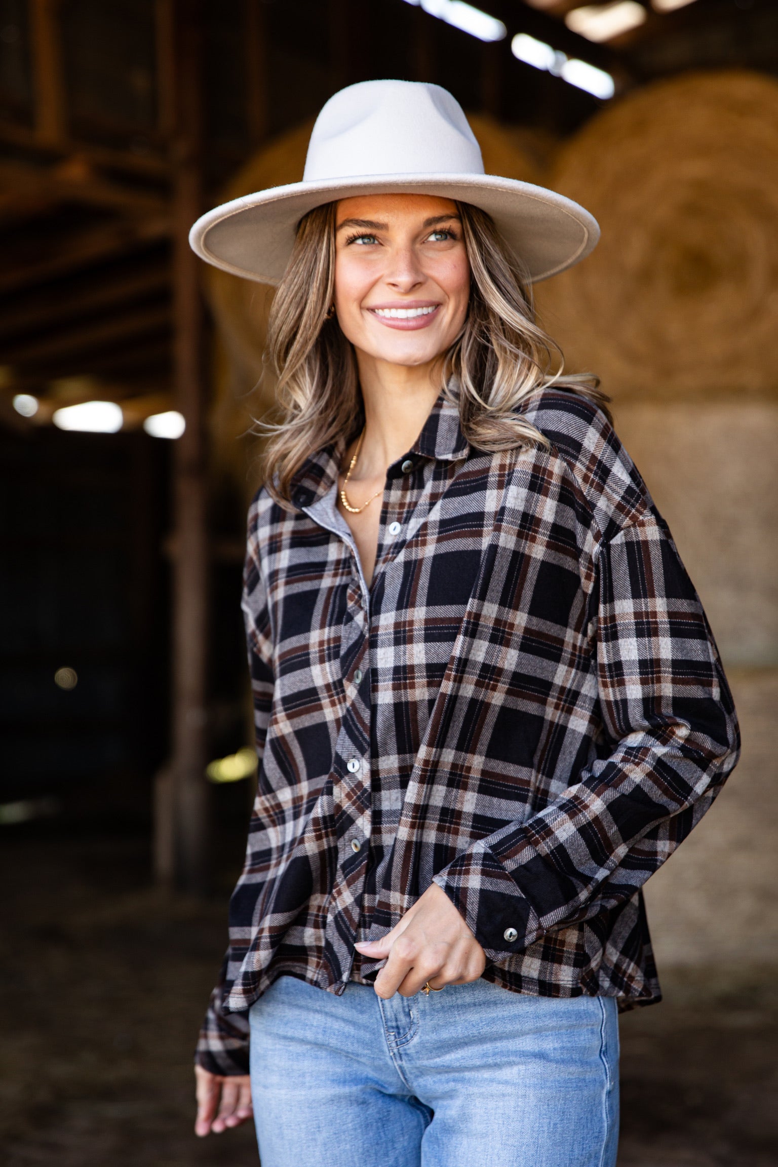 Woman wearing a plaid shirt, jeans, and a white hat in a barn setting
