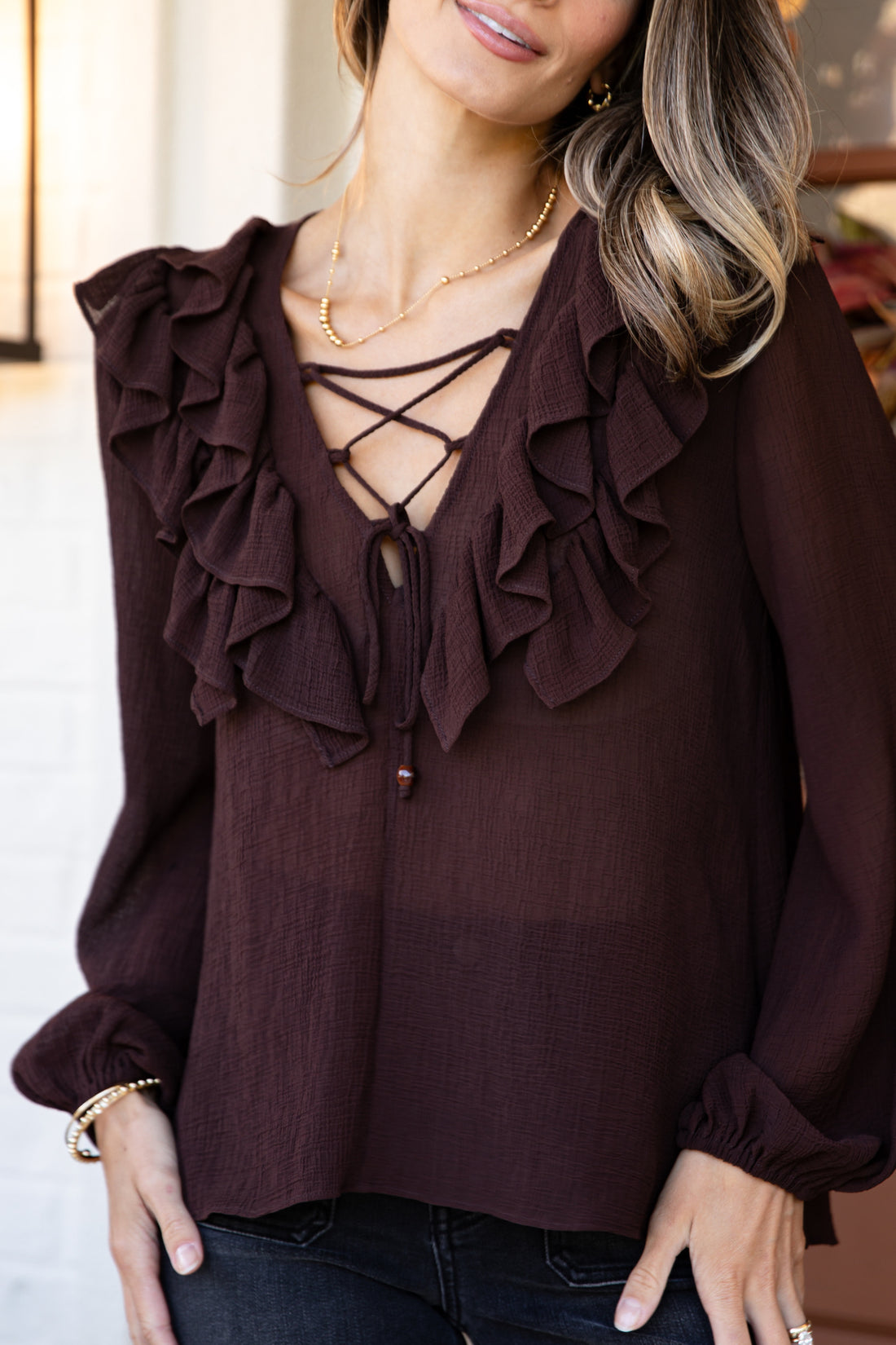 Brown blouse with ruffled details and lace-up front worn by a person.