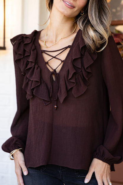 Brown blouse with ruffled details and lace-up front worn by a person.