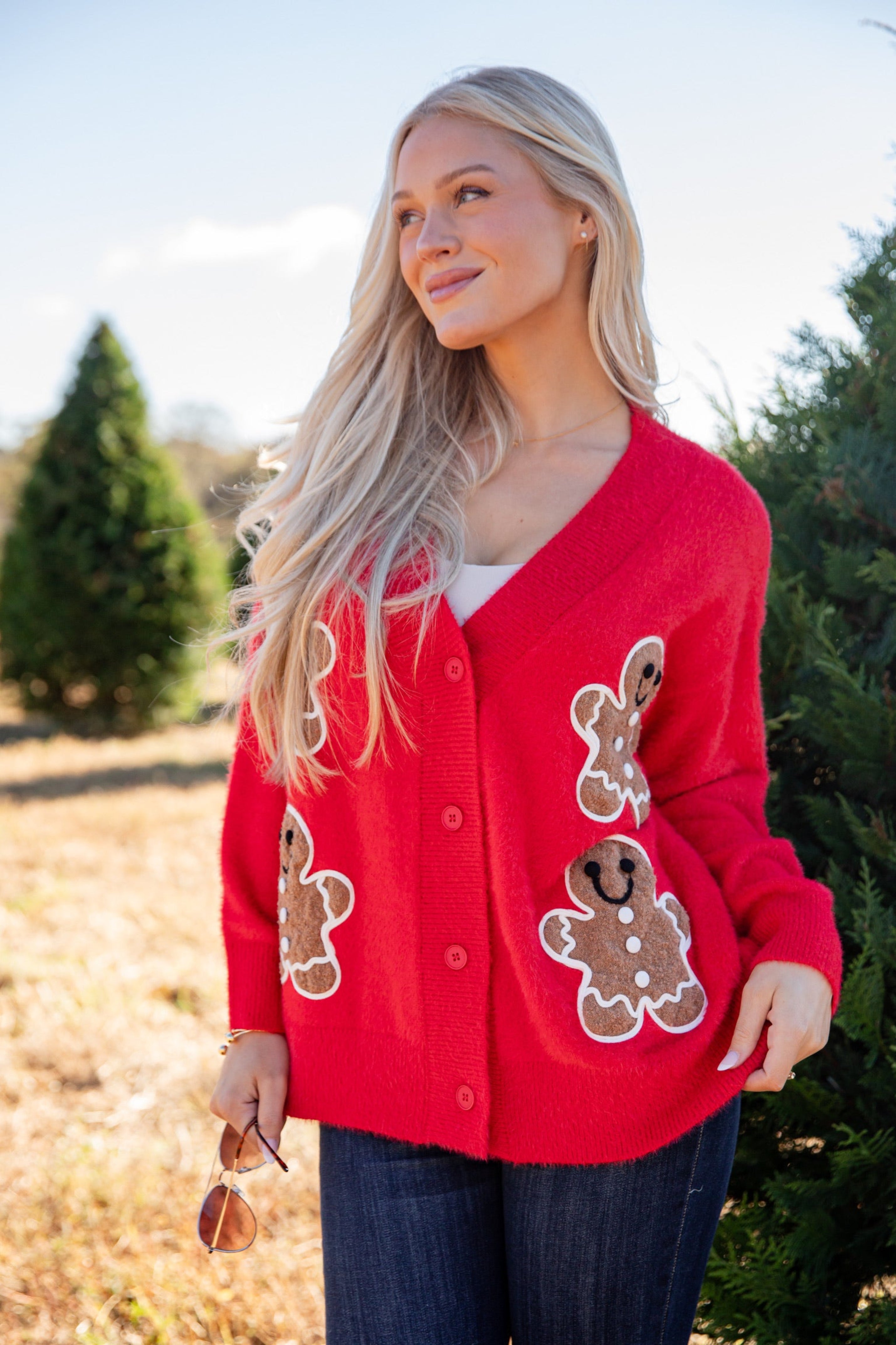 Woman wearing a red cardigan with gingerbread man patches in a Christmas tree lot.