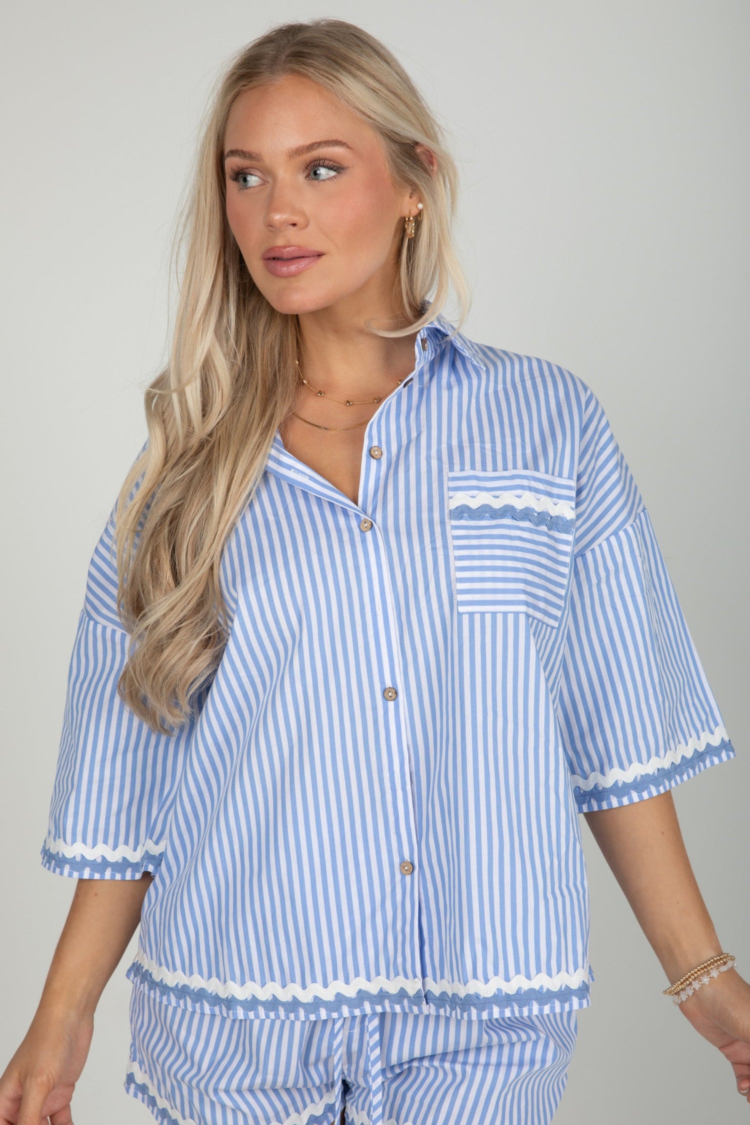 Woman wearing a blue and white striped shirt with a pocket on a gray background