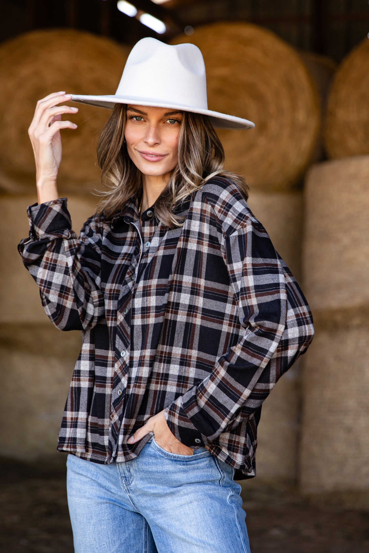 Woman wearing a plaid shirt and white hat in front of hay bales