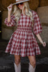 Woman wearing a red and white checkered dress with cowboy boots in front of hay bales.