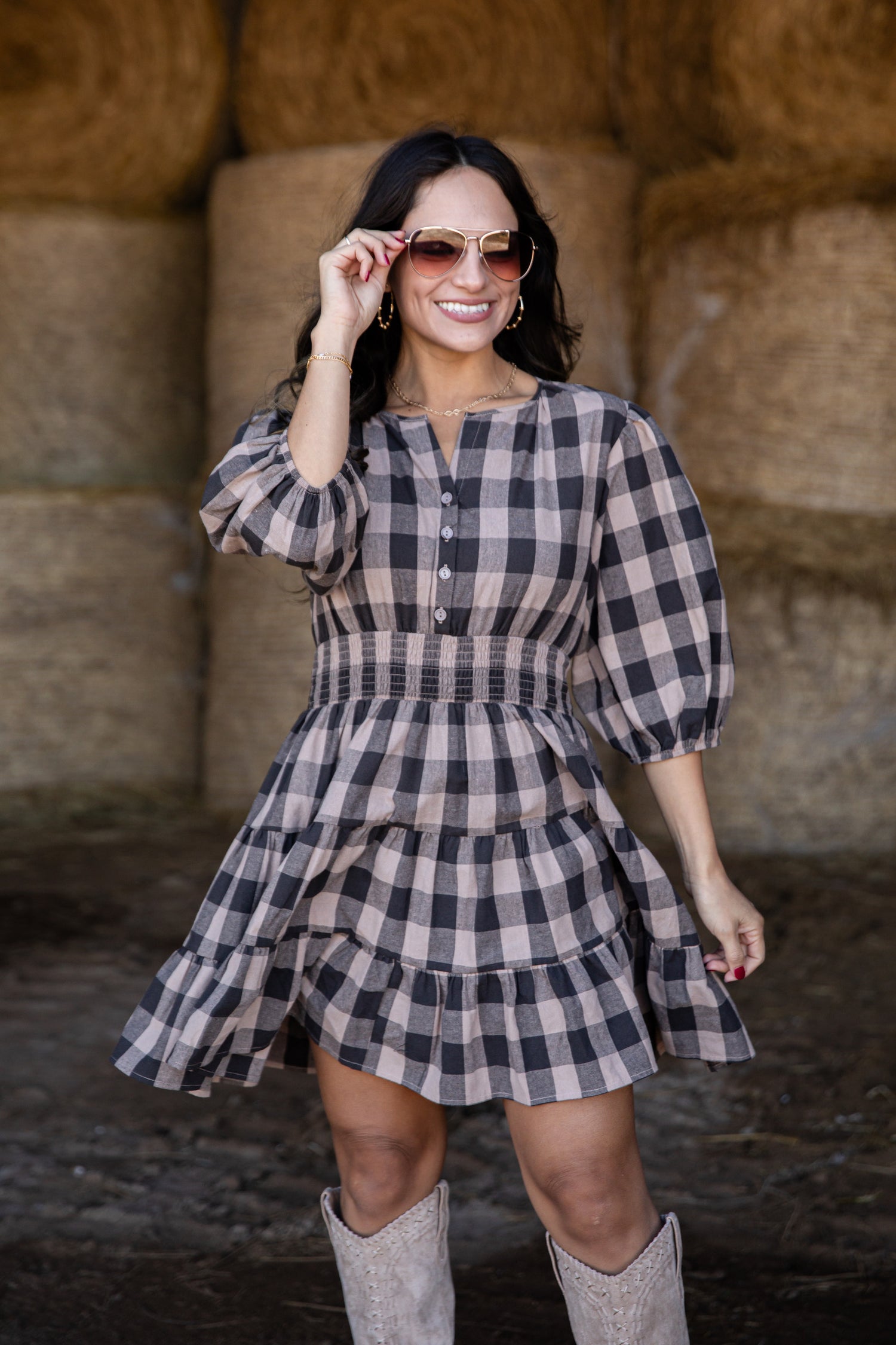Woman wearing a plaid dress and sunglasses in front of hay bales.