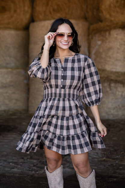 Woman wearing a plaid dress and sunglasses in front of hay bales.