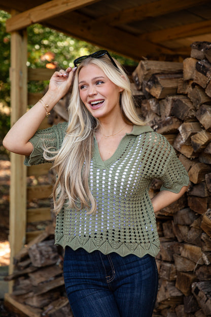 Woman wearing a green crochet top standing in front of stacked firewood.