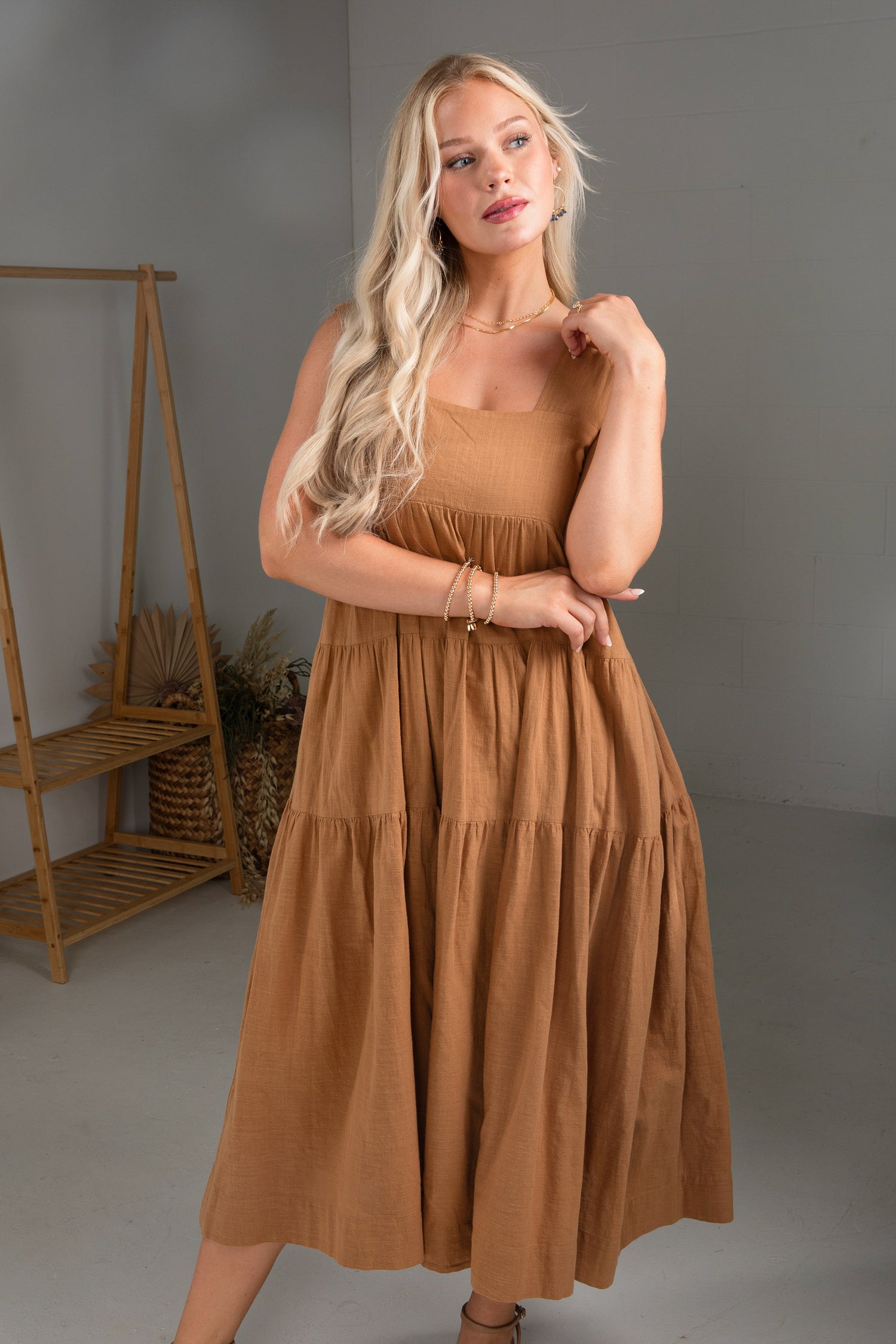 Woman wearing a brown dress in a studio setting with a wooden shelf and gray walls.