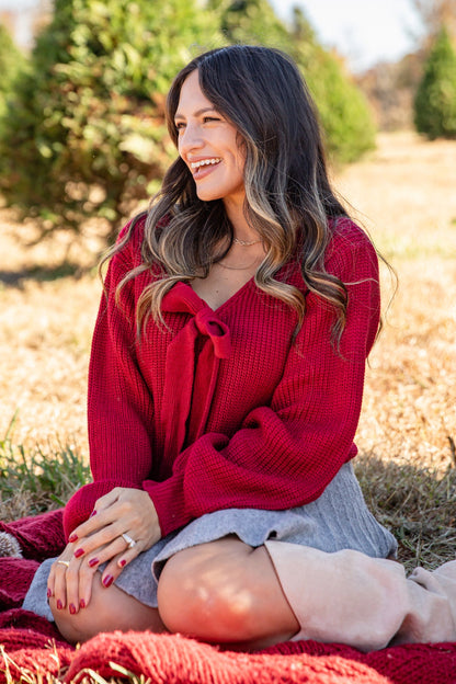 Woman in a red sweater sitting on a blanket in a Christmas tree farm.