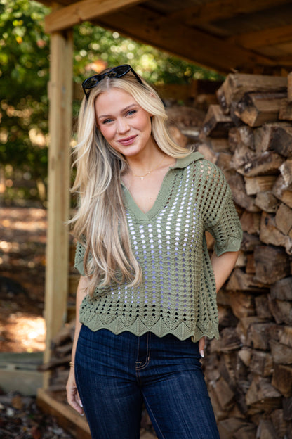 Woman wearing a green crochet top standing in front of stacked wood.