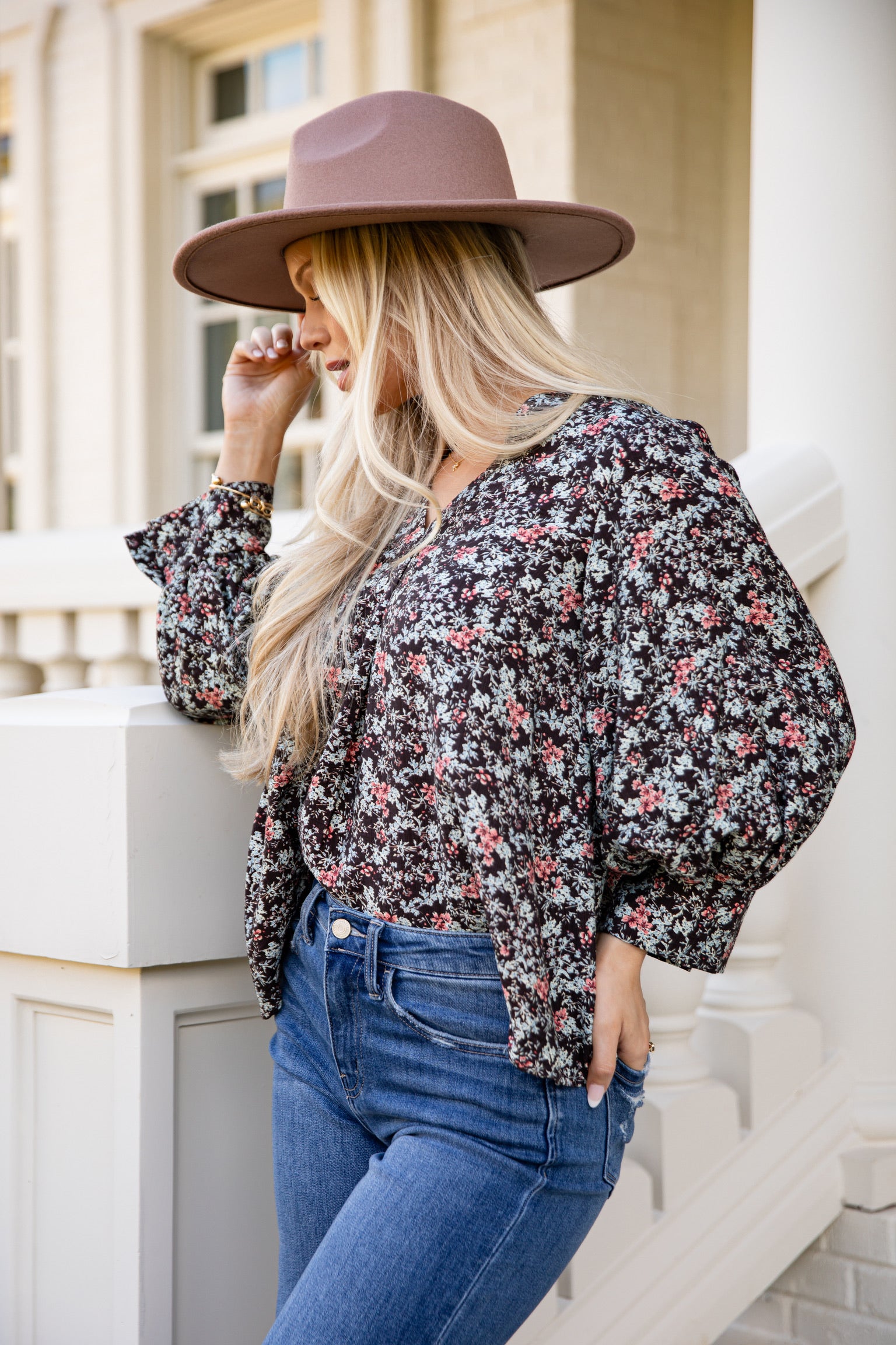 Woman wearing a floral blouse and wide-brimmed hat standing on a staircase.