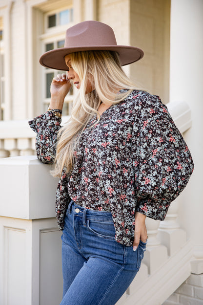 Woman wearing a floral blouse and wide-brimmed hat standing on a staircase.