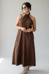 A woman modeling a brown halter-neck midi dress with a button-front closure, photographed against a plain light gray studio background.
