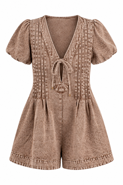 A short-sleeve romper in a washed, textured brown fabric, featuring a deep V-neckline with a tie-front closure, vertical pleated detailing on the bodice, and a flared leg.