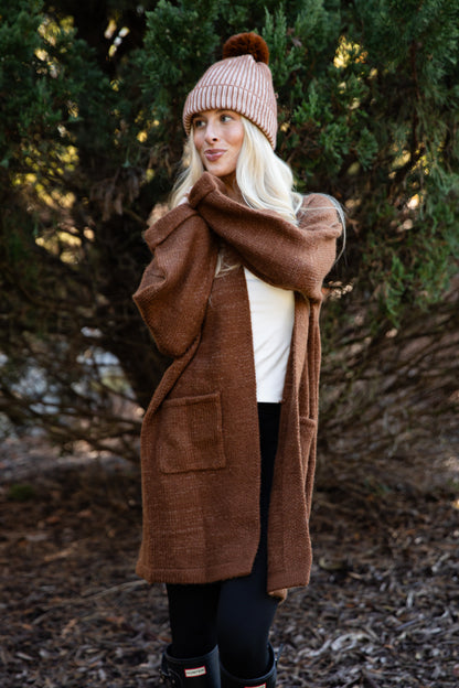 Woman wearing a brown coat and pink beanie standing in a forest setting