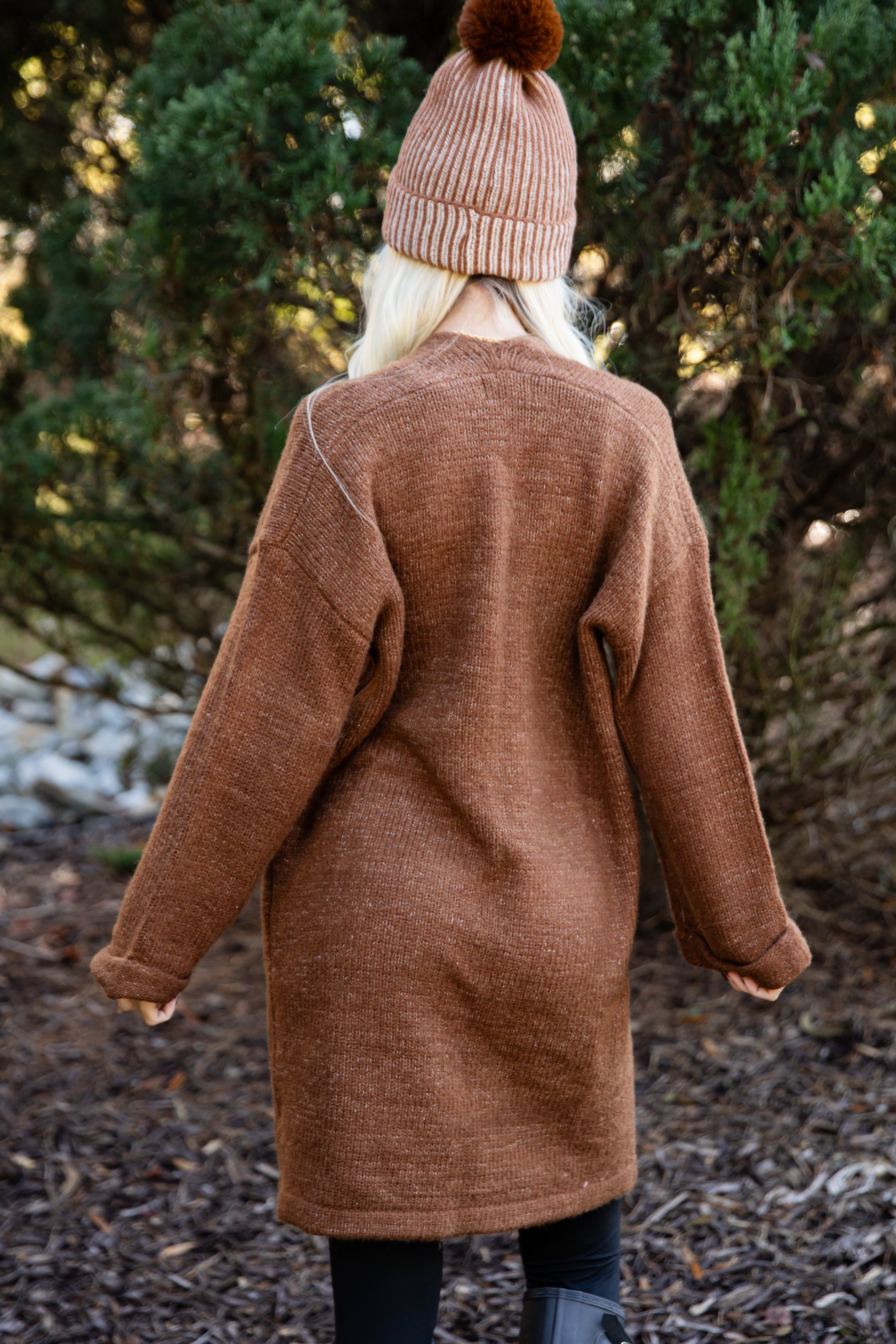 Person wearing a brown coat and pink beanie standing in a forest setting