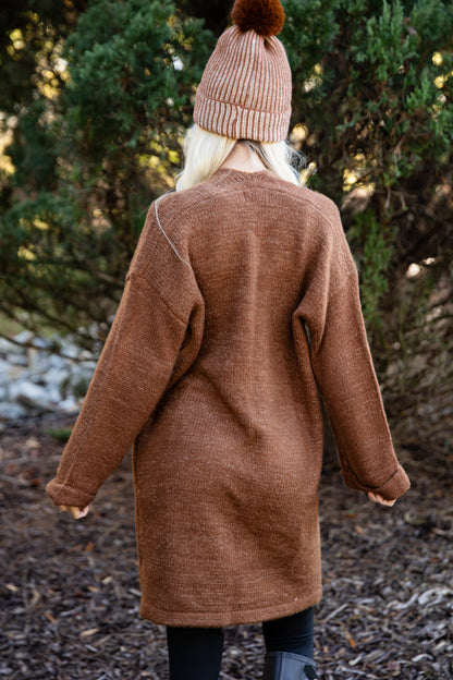 Person wearing a brown coat and pink beanie standing in a forest setting
