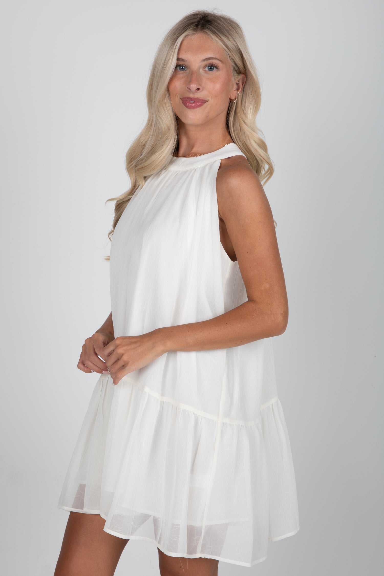 Woman wearing a white sleeveless dress against a plain background
