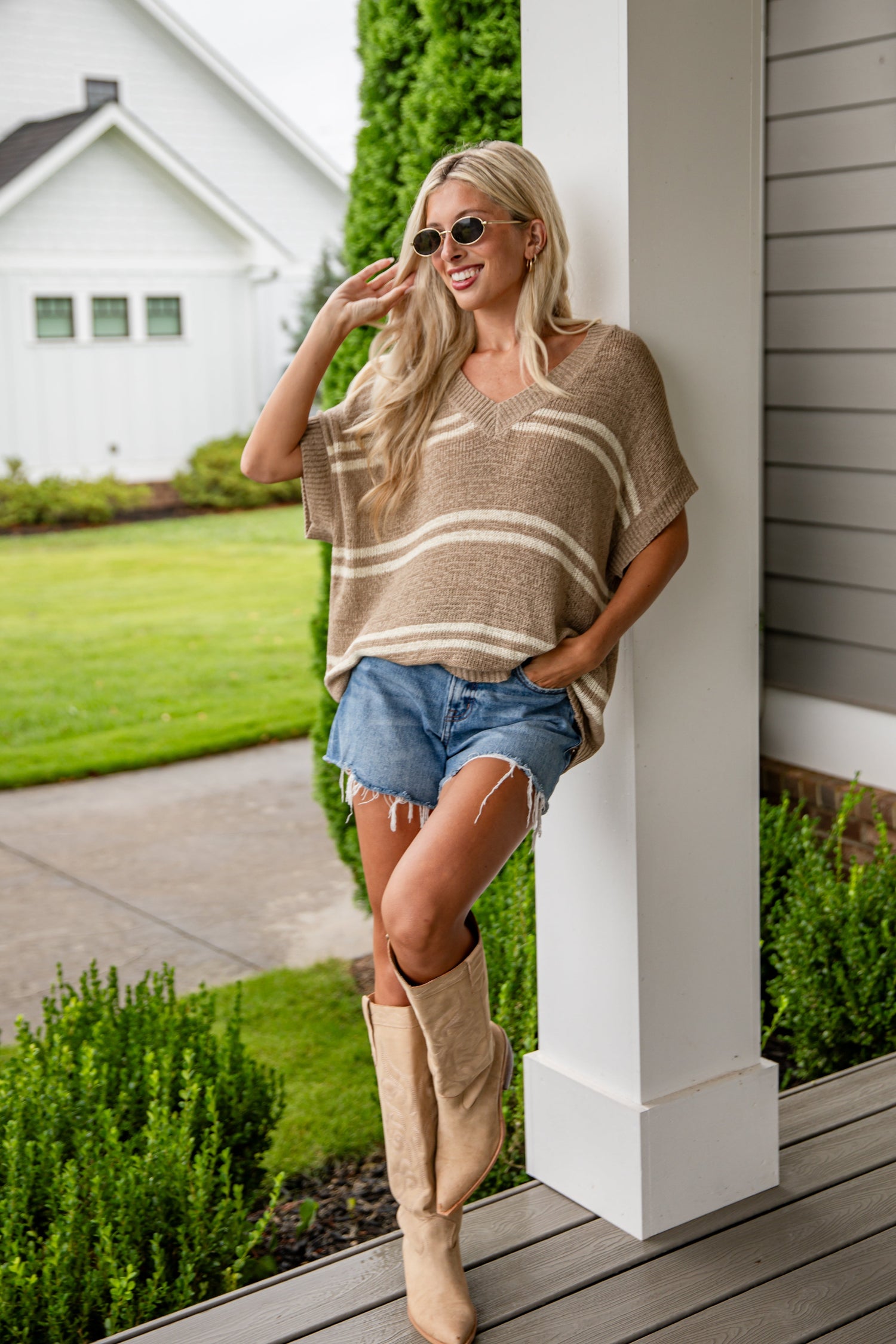 Woman in a casual outfit standing on a porch with a house in the background