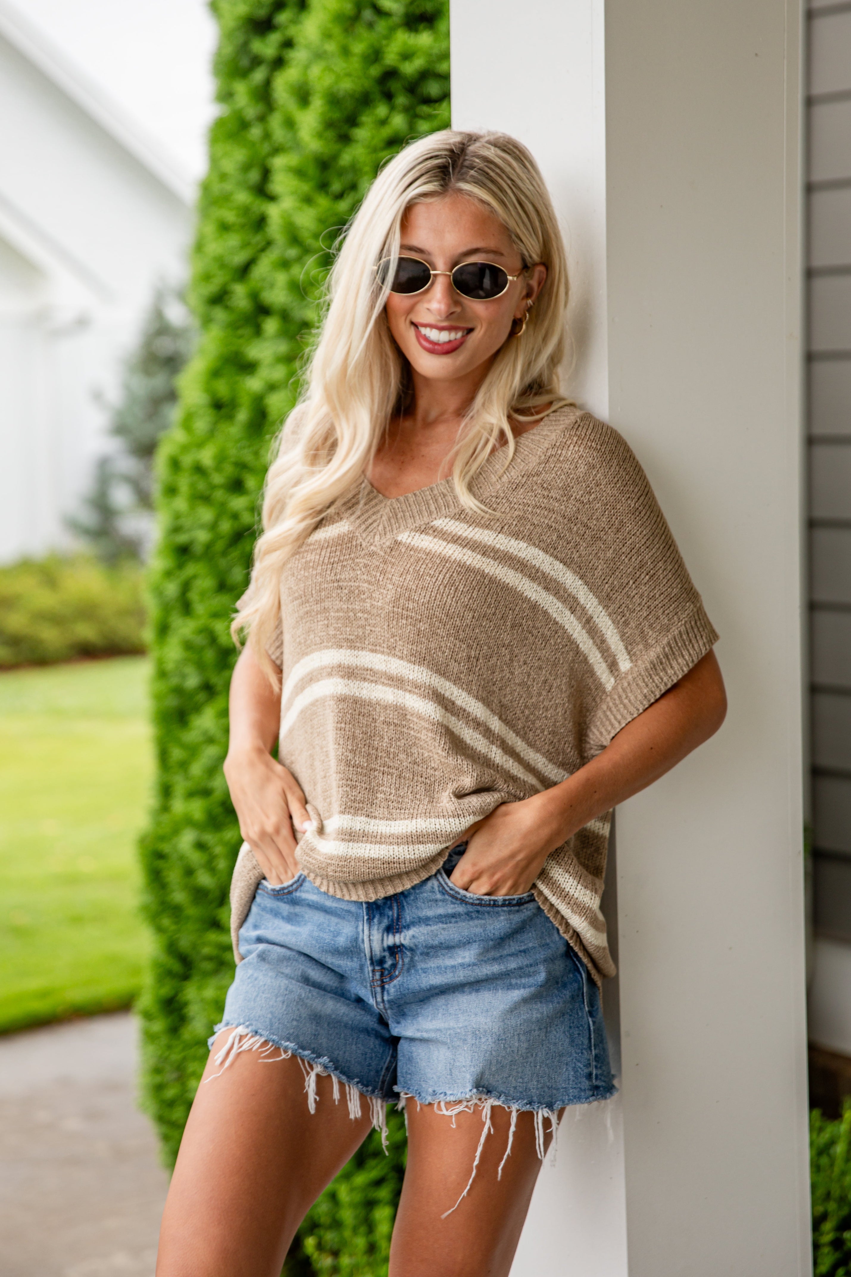Woman wearing a beige poncho and denim shorts standing outdoors.