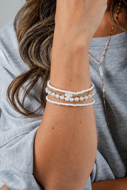 Close-up of a person wearing multiple pearl bracelets on a gray background