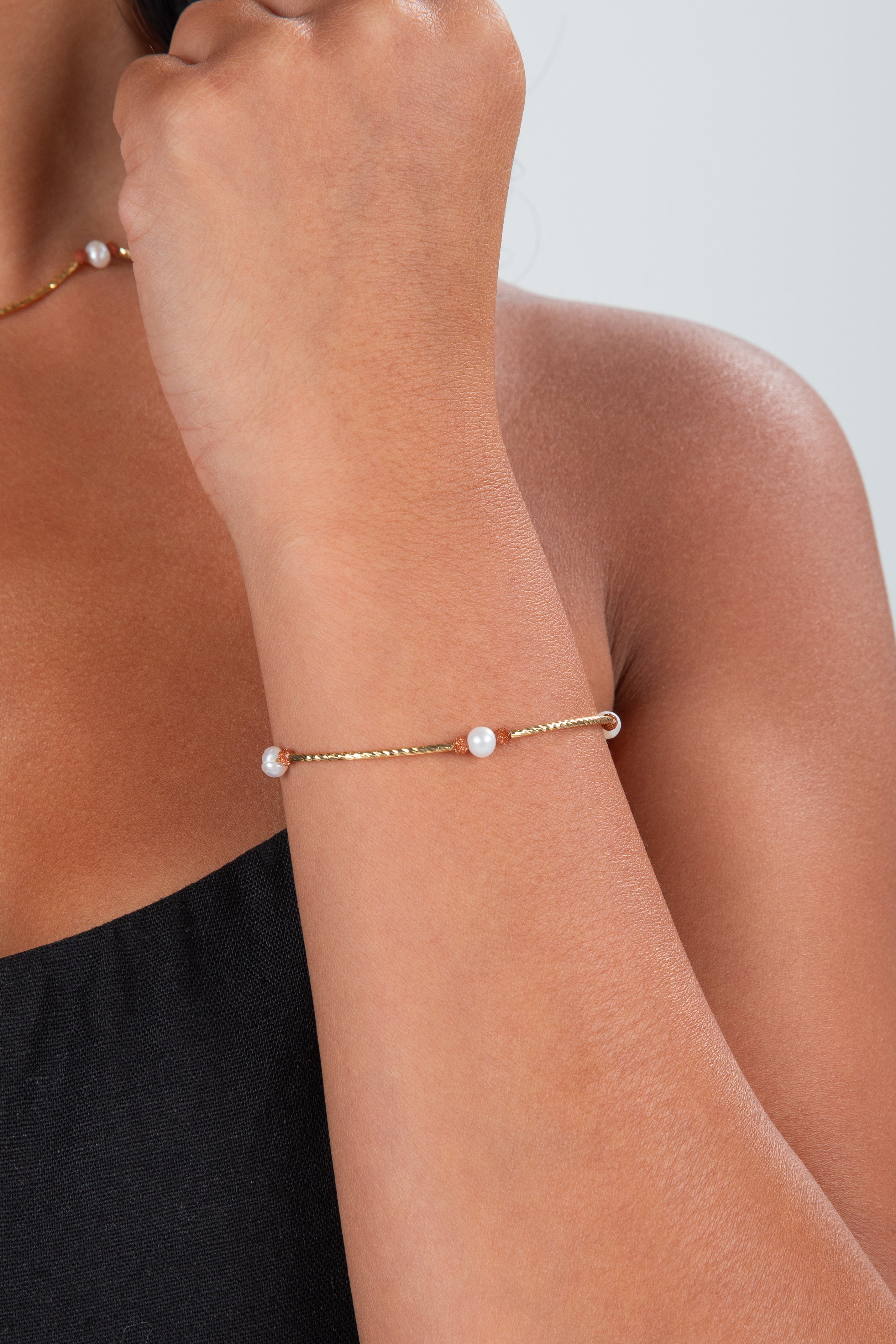 Gold bracelet with pearls on a wrist against a neutral background