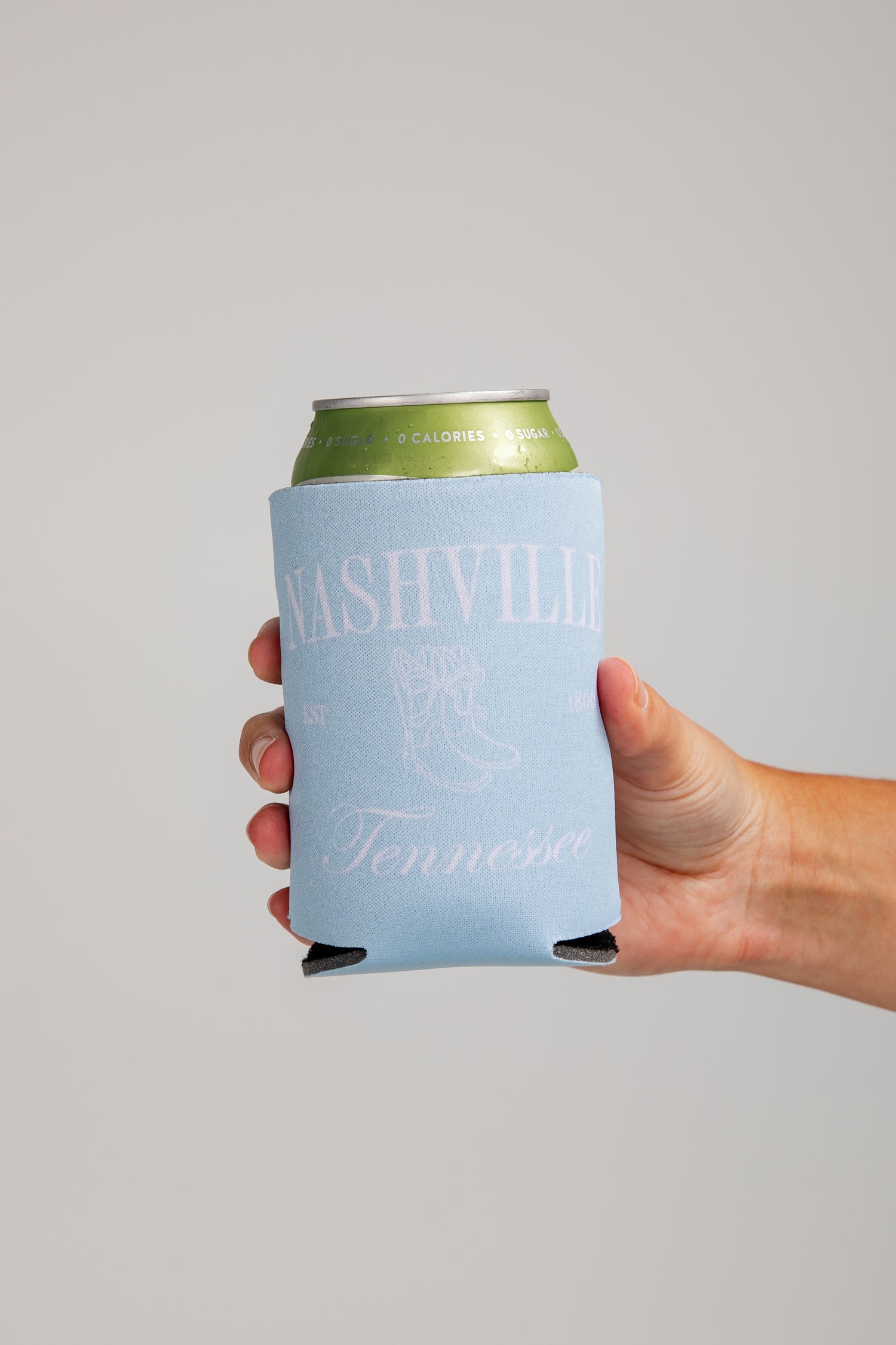 Hand holding a can with a Nashville Tennessee design on a gray background