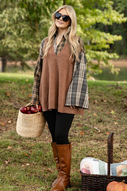 Woman in a plaid shirt and brown sweater standing outdoors with a picnic setup.