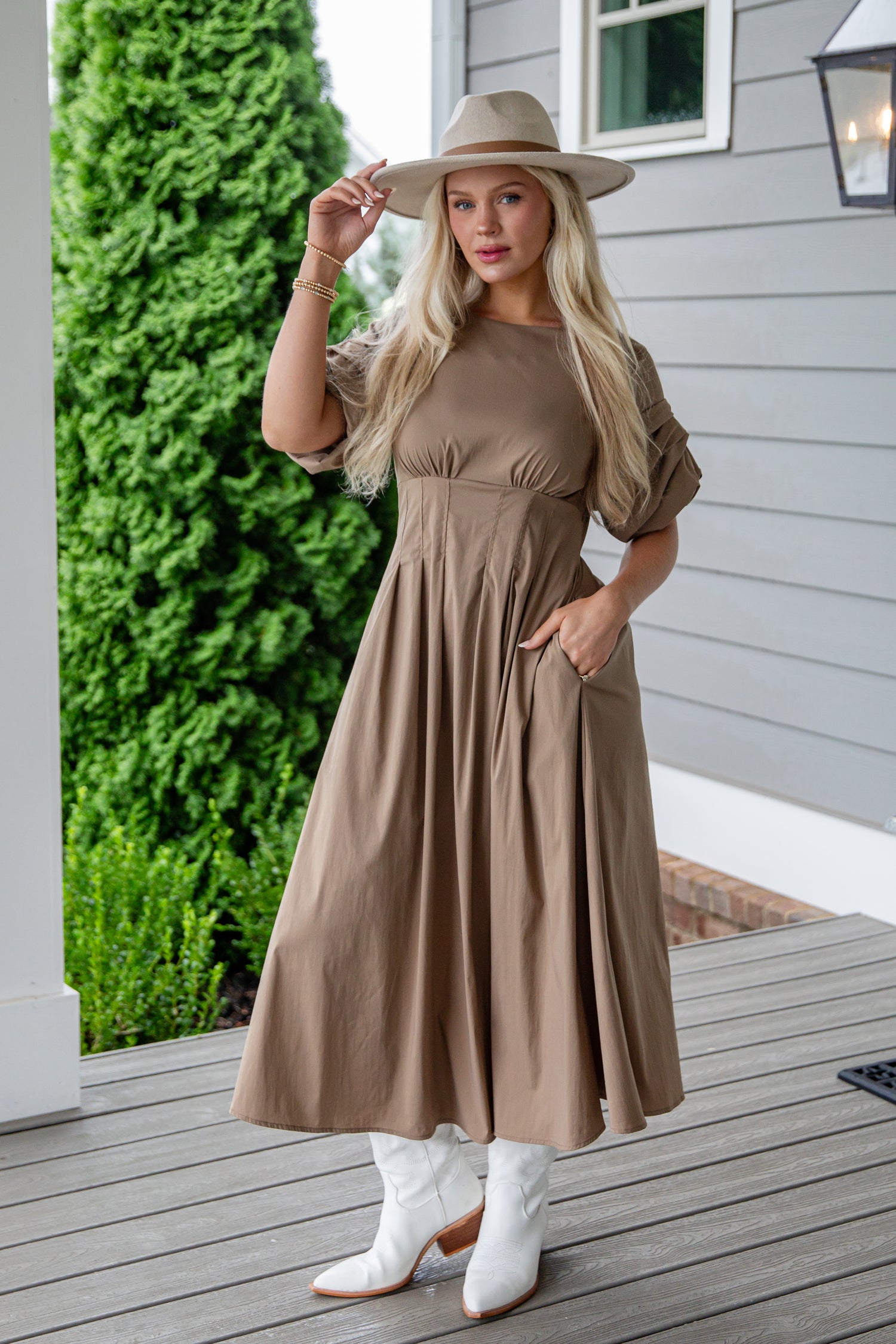 Woman in a brown dress and white boots standing on a wooden deck.