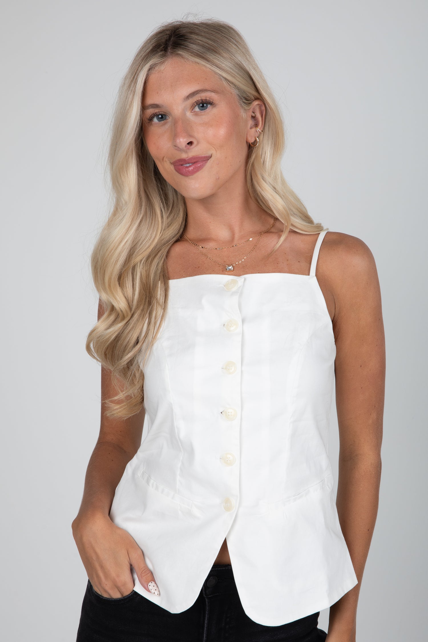Woman wearing a white sleeveless top with buttons on a plain background