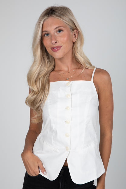 Woman wearing a white sleeveless top with buttons on a plain background