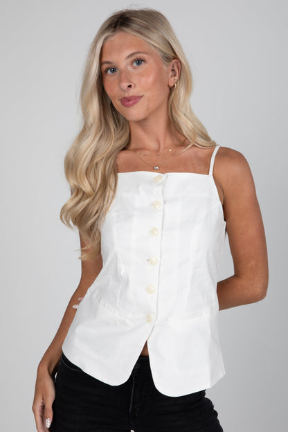 Woman wearing a white sleeveless top with buttons on a plain background