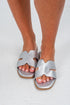 Silver sandals worn on feet against a white background