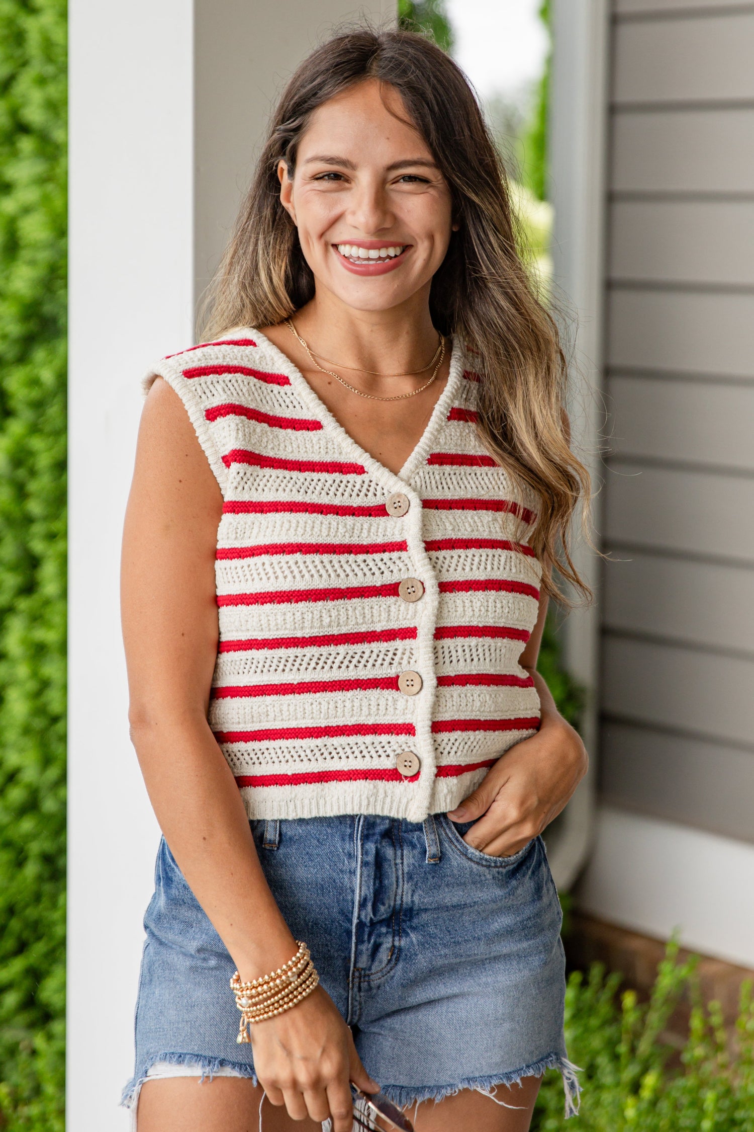 Woman wearing a red and white striped cardigan and denim shorts standing outdoors.