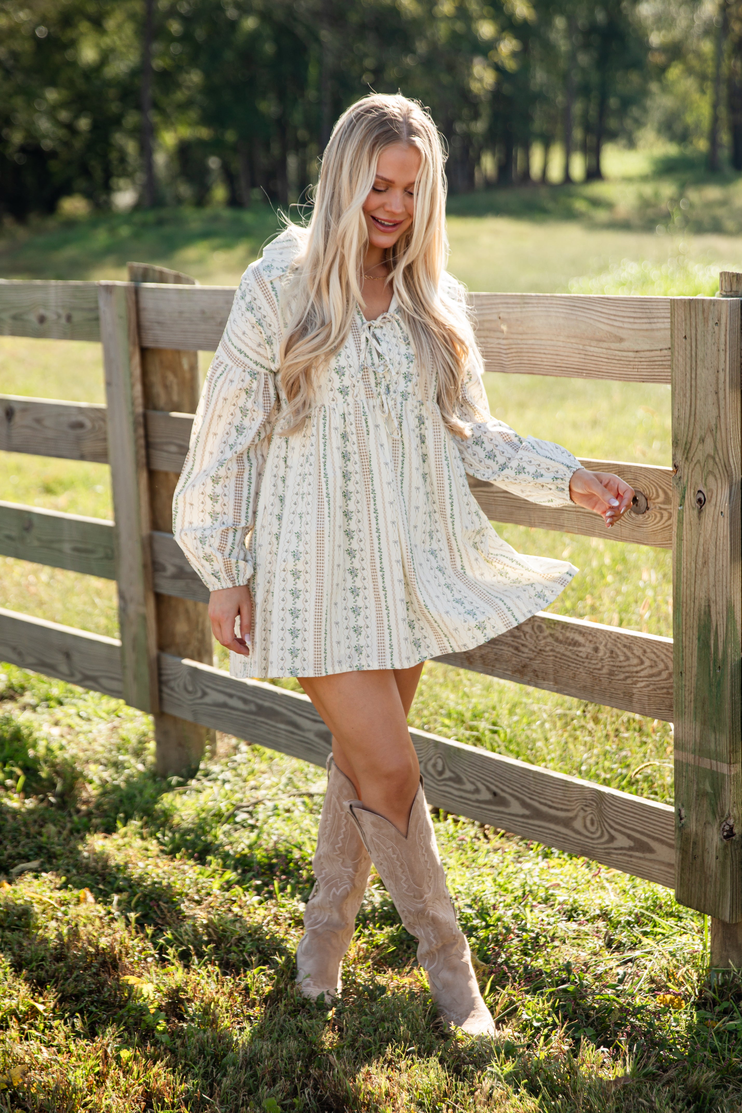 Woman in a white dress standing next to a wooden fence in a grassy field.